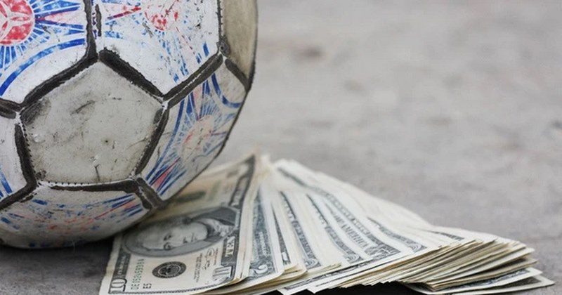 Worn soccer ball resting beside a stack of paper currency on a concrete surface